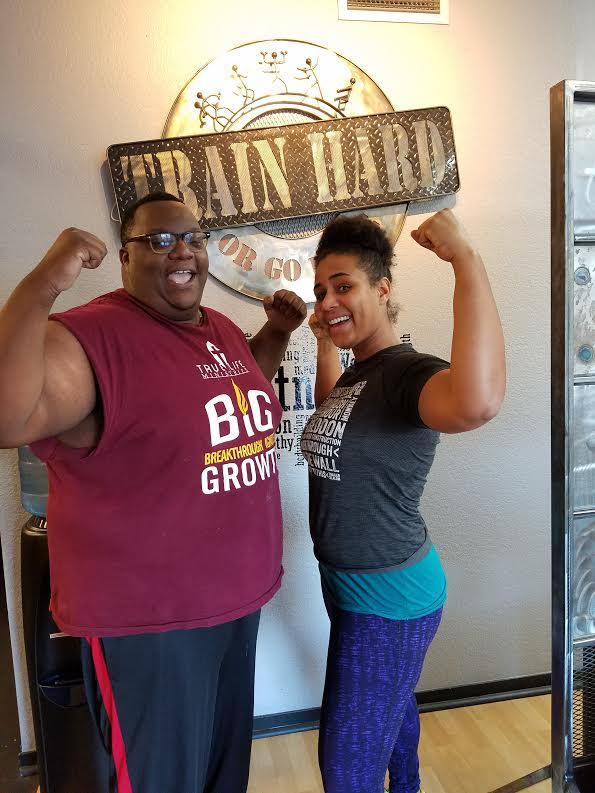 A man and a woman are flexing their muscles in front of a train hard sign.