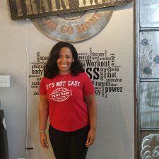 A woman in a red shirt is standing in front of a wall with words on it.