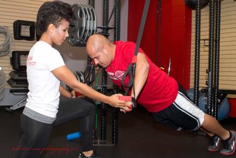 A woman is helping a man do push ups in a gym