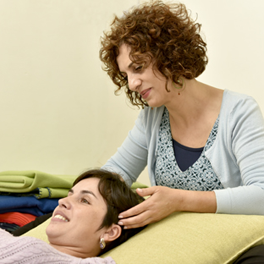 אישה מקבלת עיסוי ראש מאישה אחרת בחדר בהיר. המטופלת שוכבת על כרית ומחייכת.