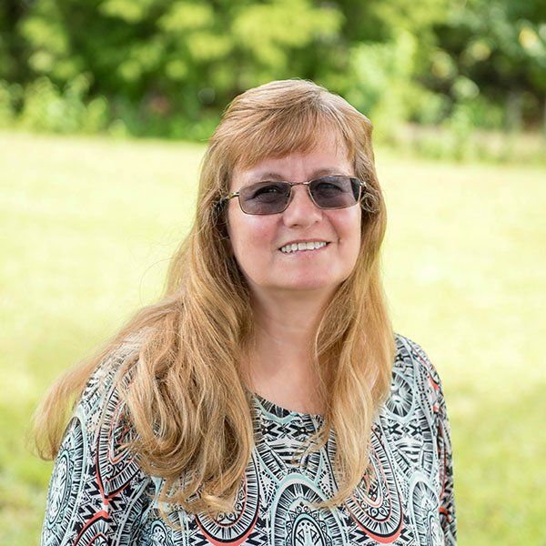 Woman with long blonde hair and glasses smiles outdoors.