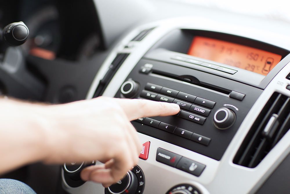 Doigt d'une personne appuyant sur un bouton d'autoradio. Écran orange, boutons noirs, panneau argenté.