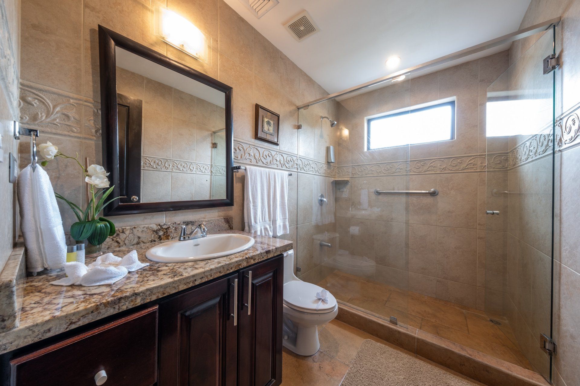 A bathroom with a sink , toilet , mirror and walk in shower.