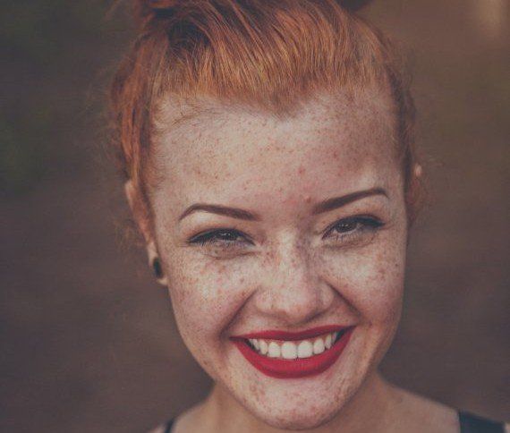 Smiling red-haired woman with freckles and bright red lipstick against a blurred background