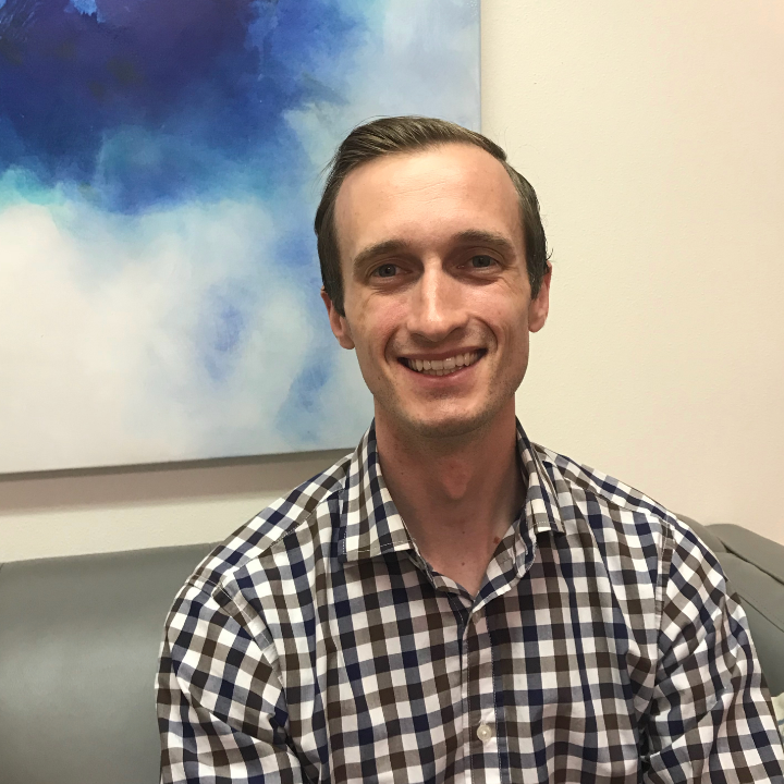 Smiling person in a checkered shirt seated indoors against a blue-and-cream abstract wall painting