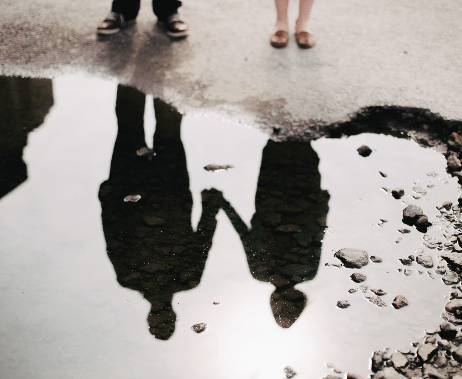 Two people’s reflections holding hands in a rain puddle on wet pavement