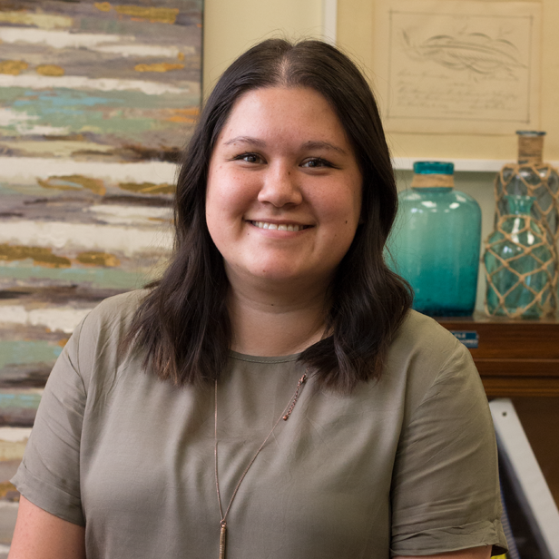 Smiling person in a gray shirt seated indoors, with abstract wall art and blue decorative vases behind them.