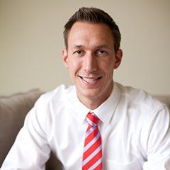Smiling person in a white shirt and red striped tie sitting indoors on a couch