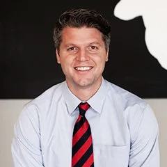 Smiling man in a light blue shirt and red striped tie against a black-and-white background