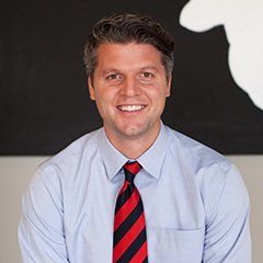 Smiling man in a light blue shirt and red striped tie against a black-and-white background