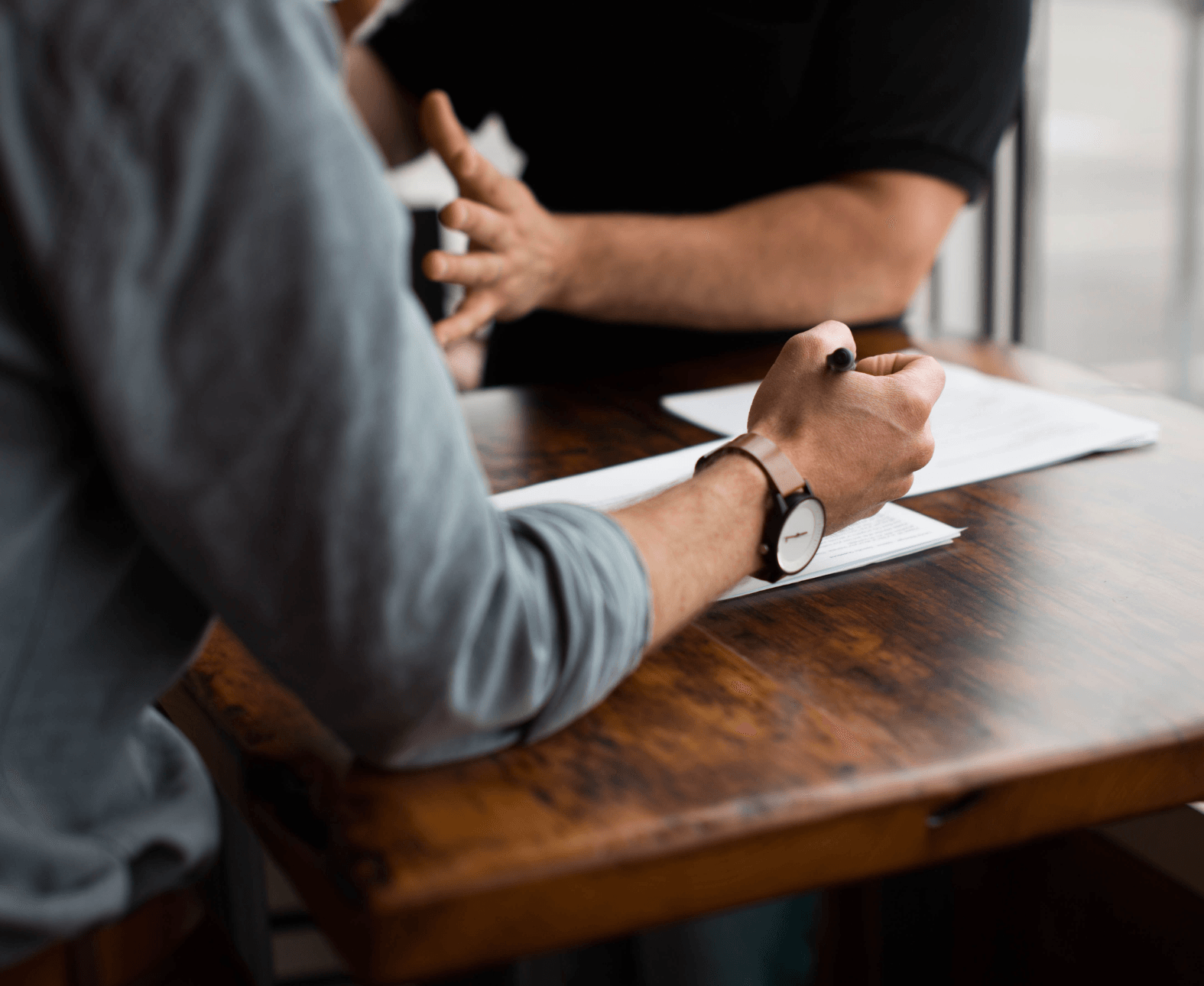 Two people in a meeting, one writing on paper at a wooden table