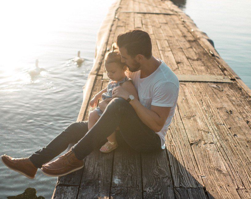 Man and child sitting on a wooden dock by the water in warm sunlight