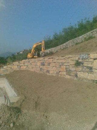 muro in pietra con scavatrice dietro