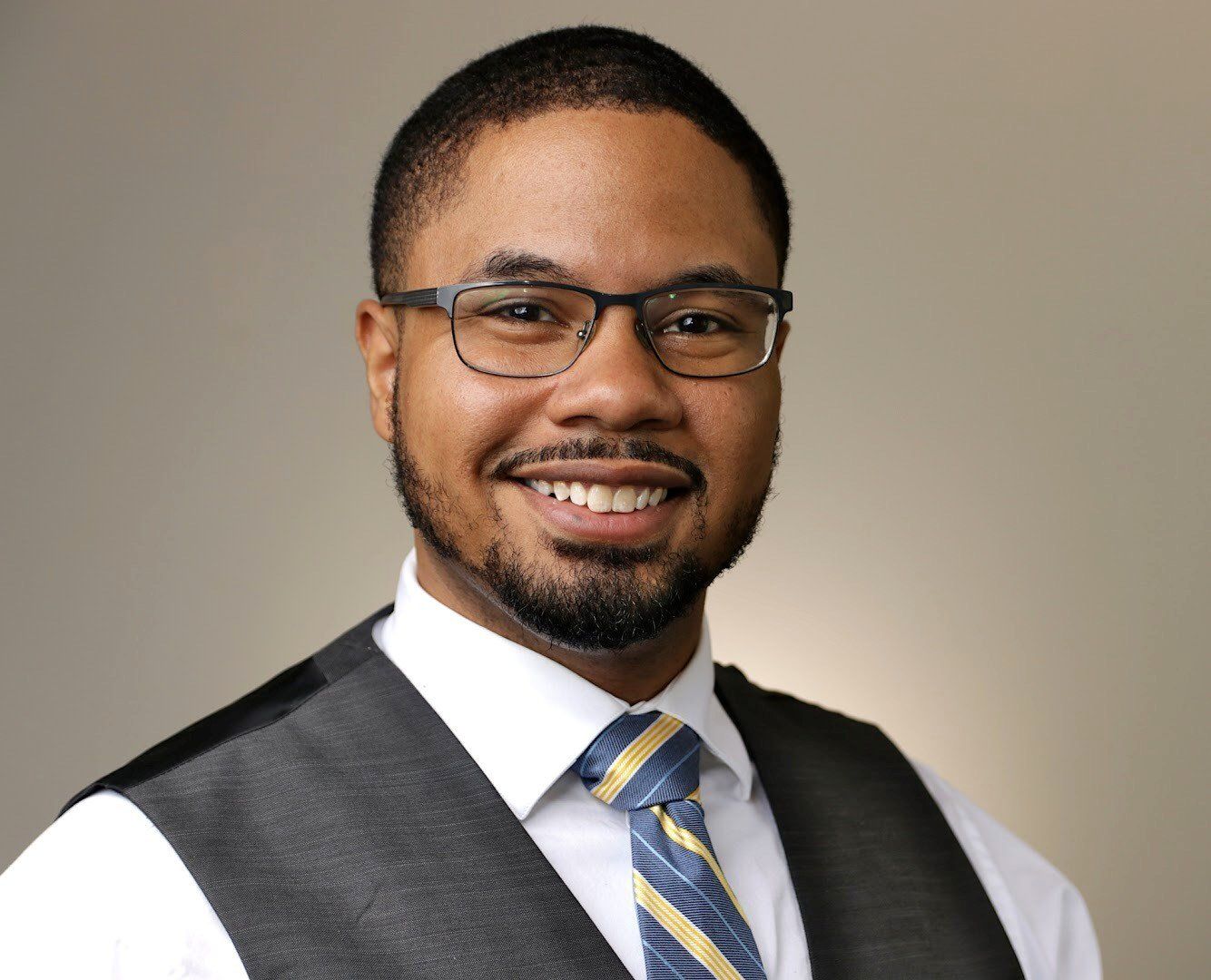 A man wearing glasses and a vest and tie is smiling for the camera.