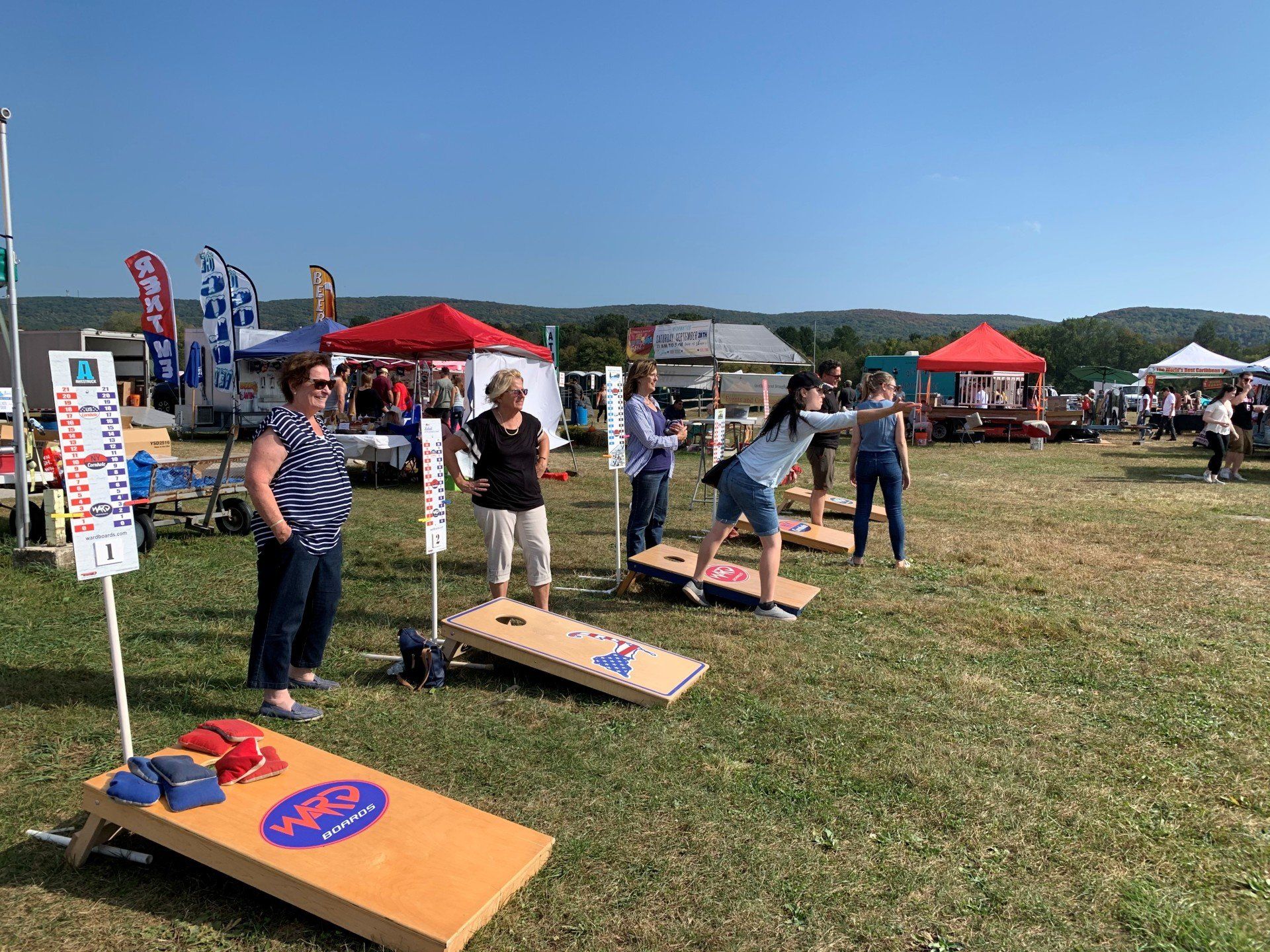 A group of people are playing cornhole in a field.