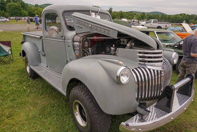 A gray truck with the hood up is parked in a grassy field.