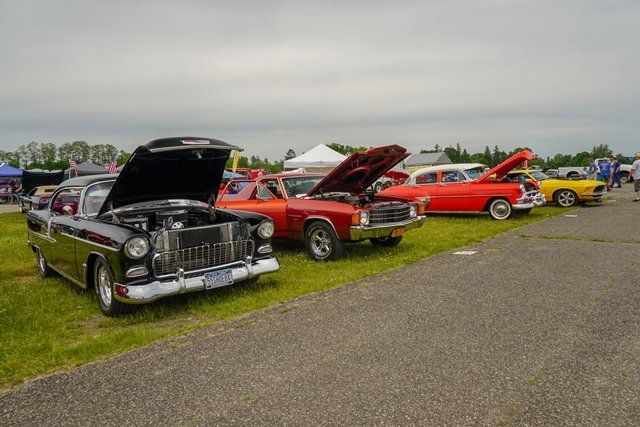 A row of cars are parked on the side of the road at a car show.