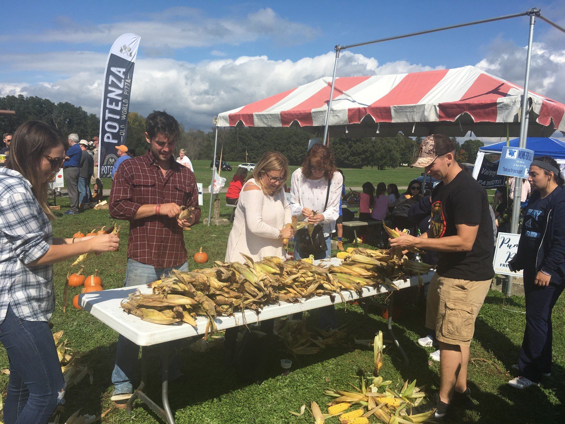 A group of people are standing around a table with corn on it.