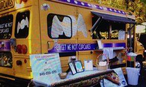 A yellow and purple food truck is parked next to a table.