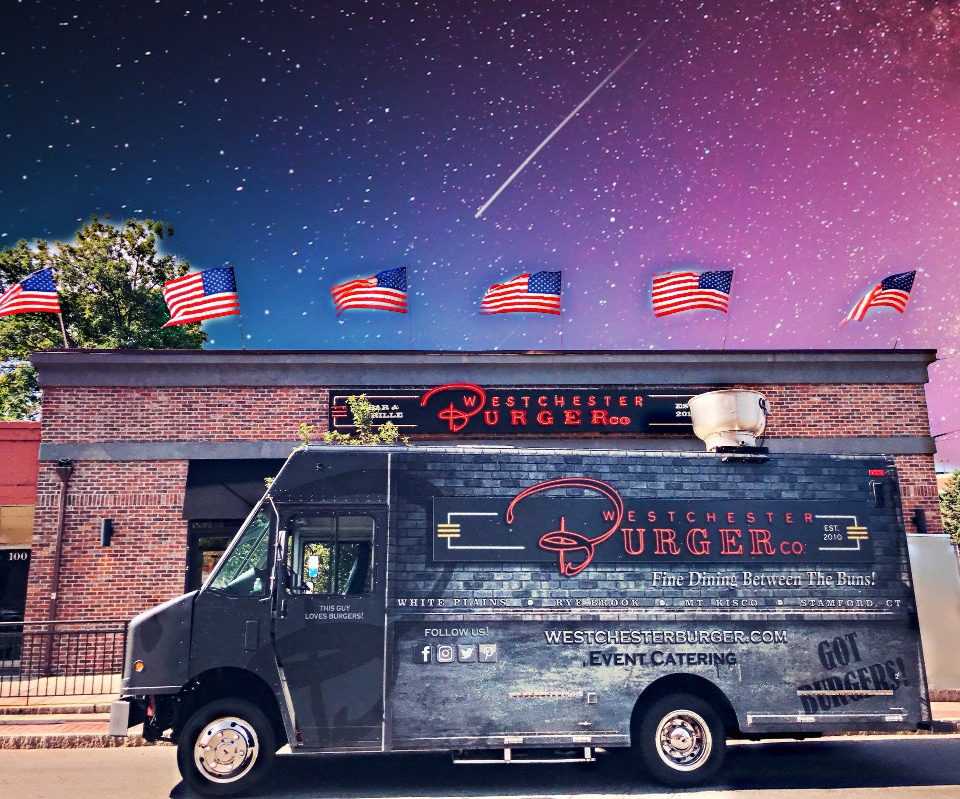 A burger truck is parked in front of a brick building