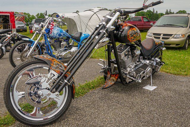 A chopper motorcycle is parked in a parking lot next to a car.