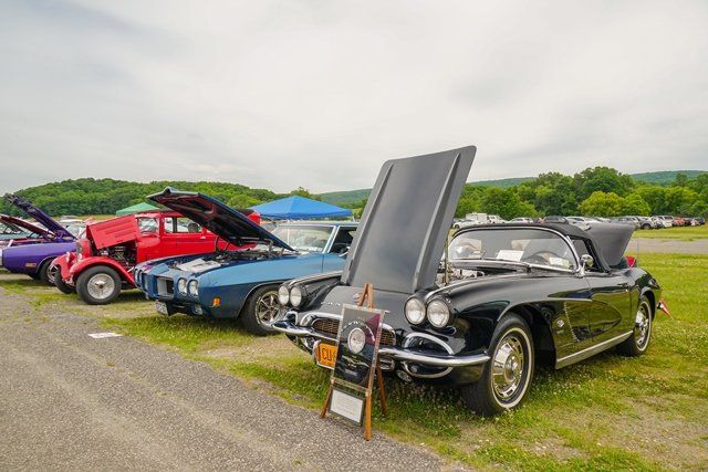 A row of classic cars are parked in a grassy field at a car show.