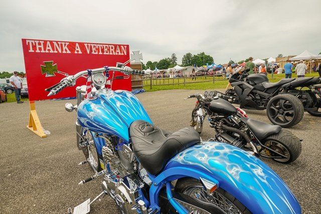 A blue motorcycle is parked in front of a sign that says thank a veteran