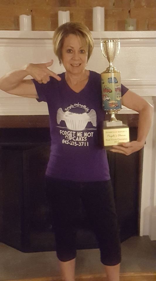 A woman in a purple shirt is holding a trophy