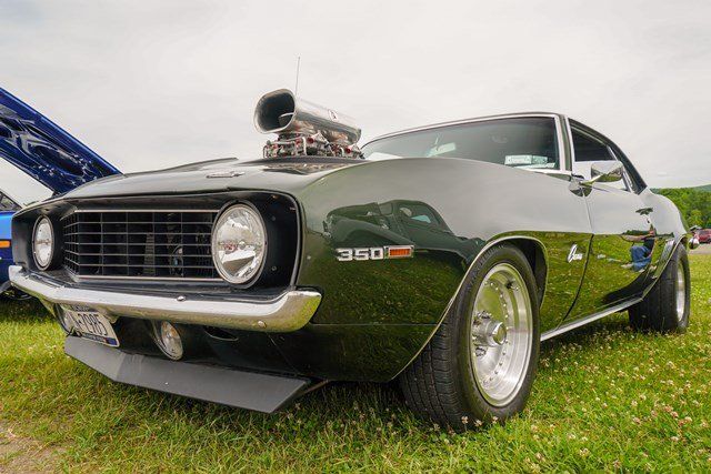 A black muscle car is parked in the grass at a car show.