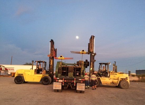 Two forklifts loading equipment onto flatbed trucks