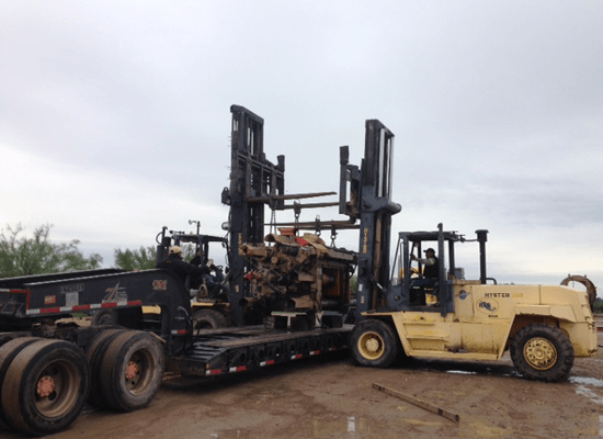 Two forklifts lowering heavy equipment onto flatbed truck