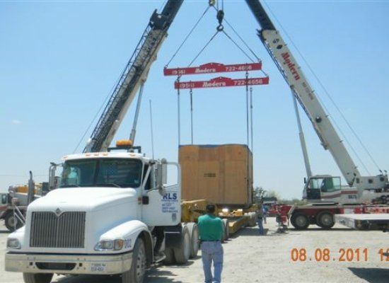 Two cranes placing oversize material onto a flatbed truck