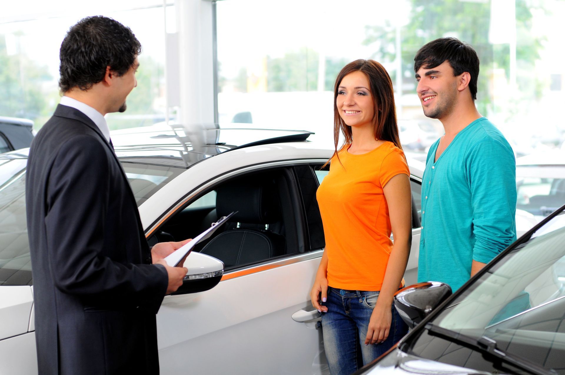 Car salesman showing a couple a car in a dealership; the couple smiles.