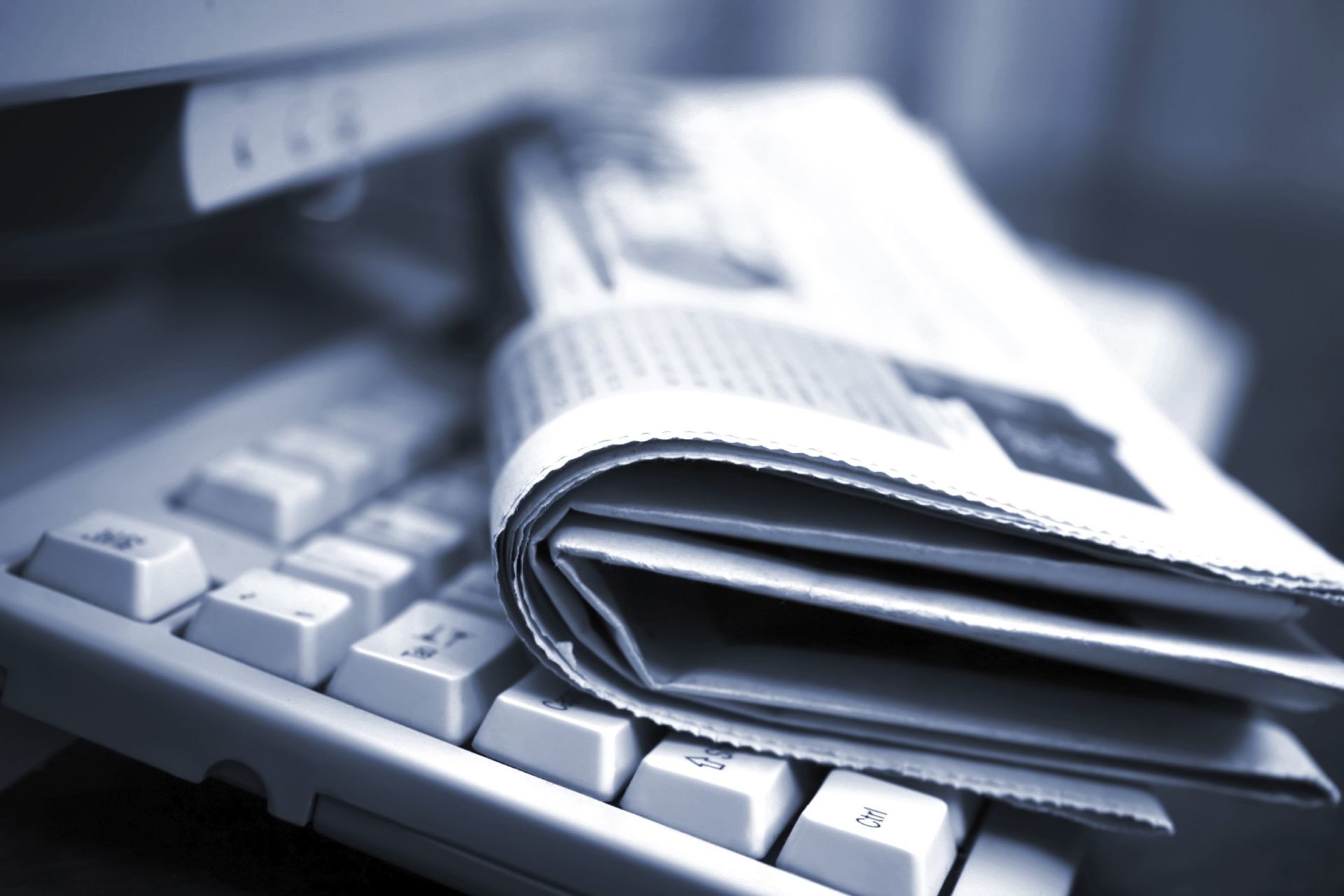 A newspaper is laying on top of a computer keyboard