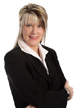 A woman in a black suit and white shirt is standing with her arms crossed.