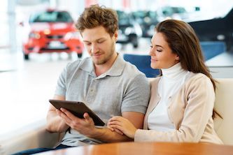 A man and a woman are looking at a tablet in a car showroom.