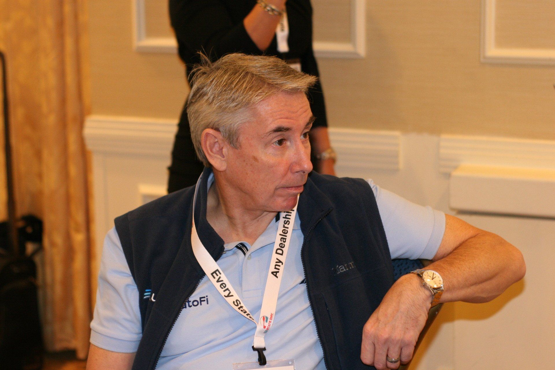 Man in blue vest and polo shirt, looking to the side, wearing a name tag.