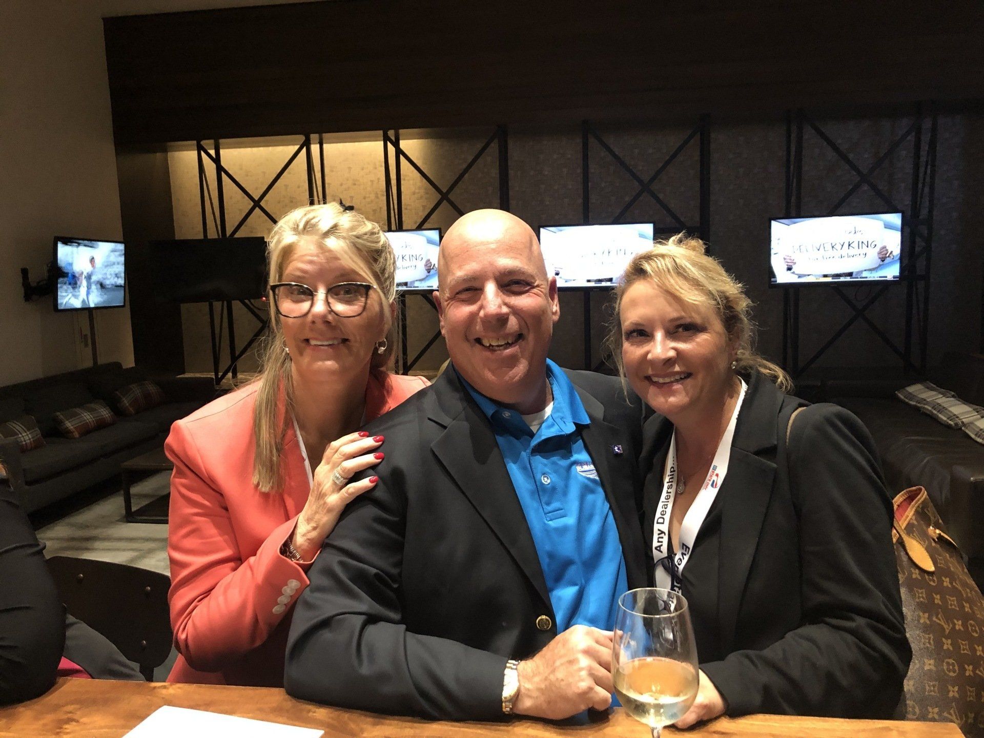 Three people smiling together, posing by a bar. 