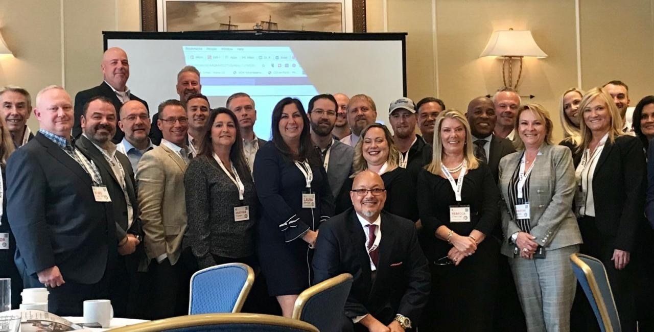 Group of people at a conference, posing in front of a screen and tables.
