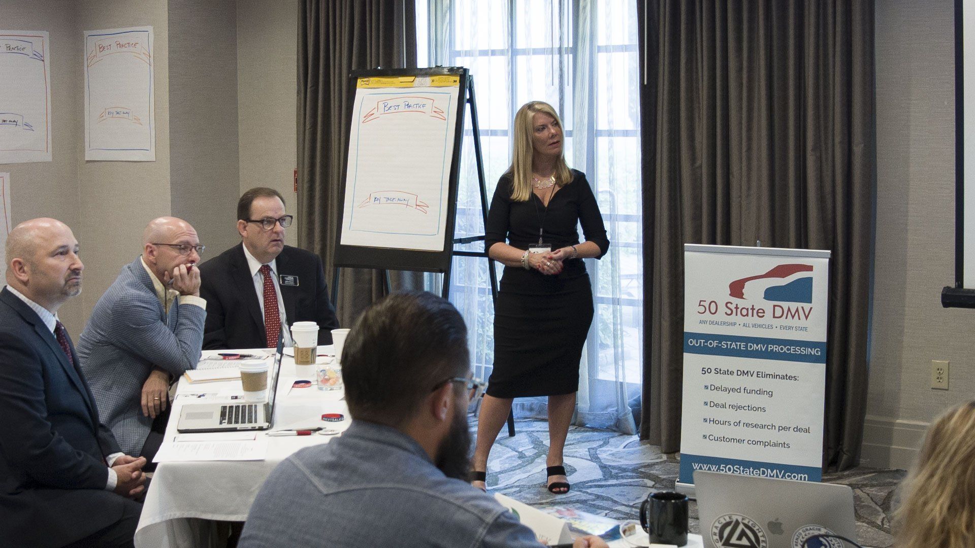 Woman presenting to a group in a conference room, with a flip chart and banner.