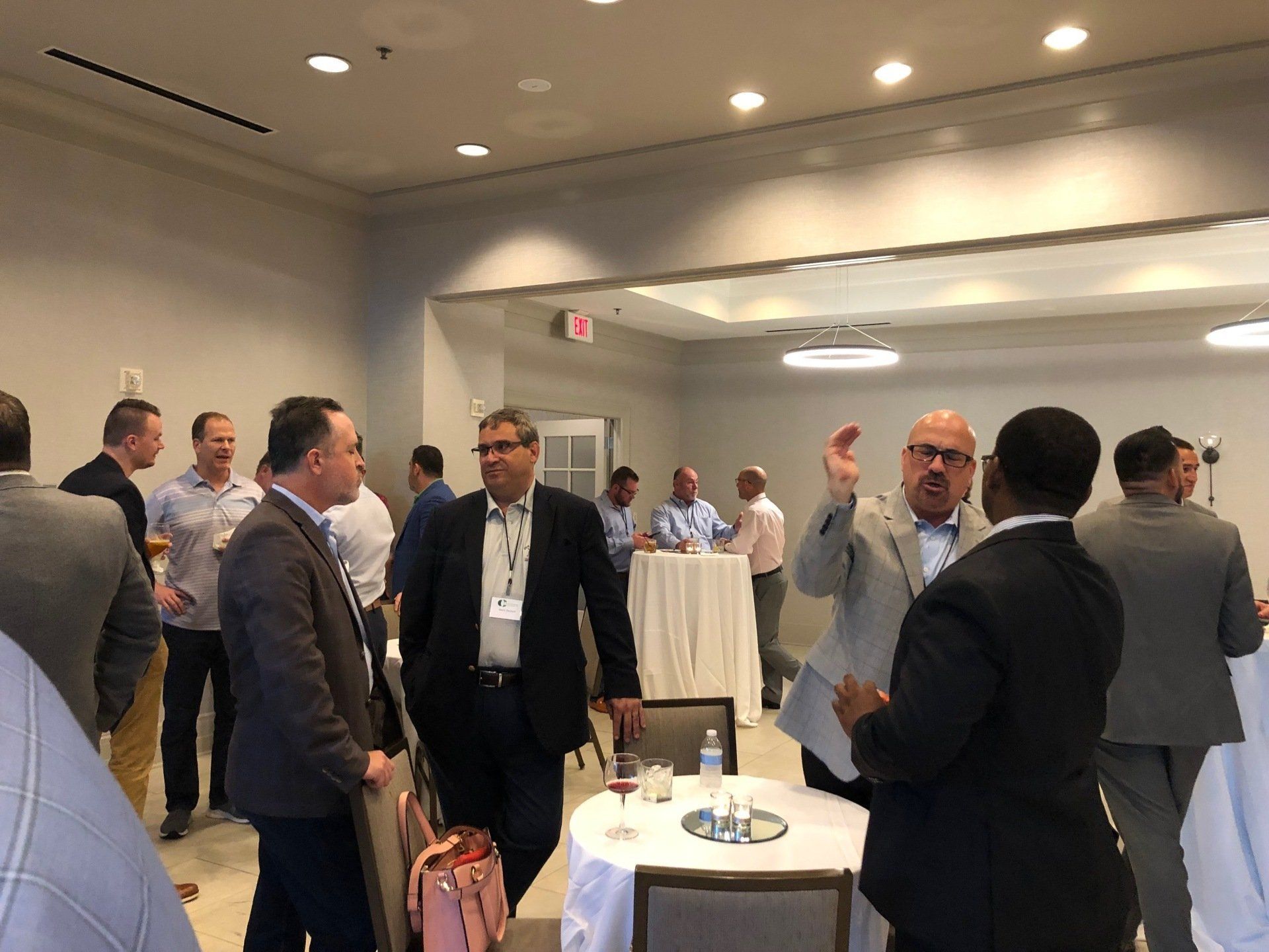 People in suits and business casual attire mingling in a brightly lit room.