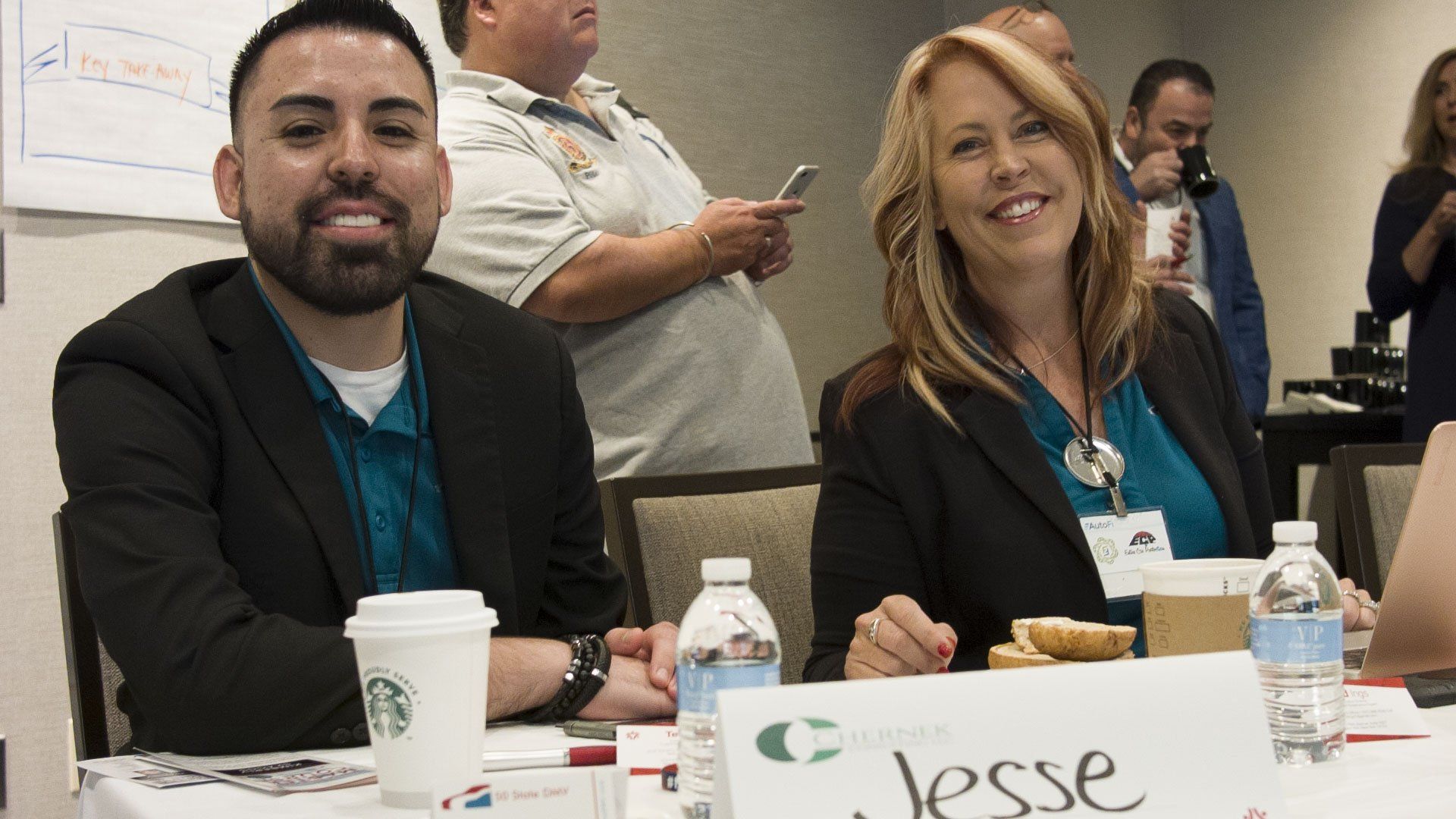 Two people smiling at a table, one with a Starbucks cup and name tag 