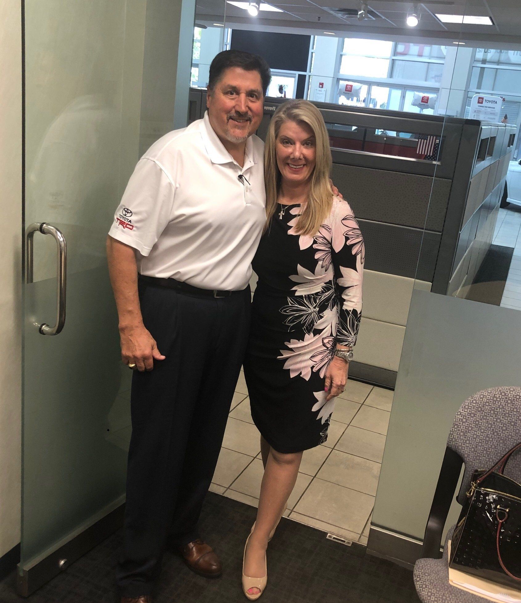 Man in white polo and woman in floral dress posing in an office.