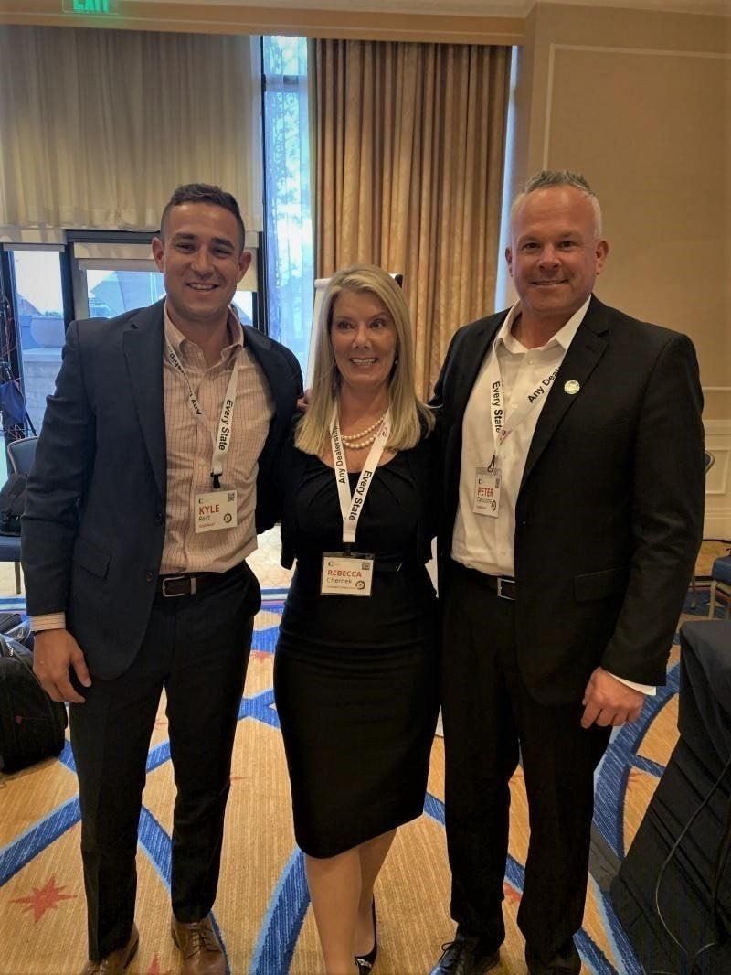 Three people in business attire pose for a photo at an event.