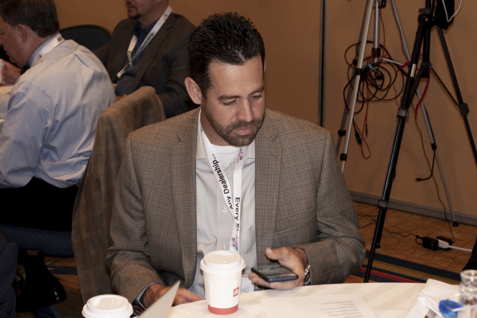 Man in blazer looking at his phone at a table with a coffee cup.