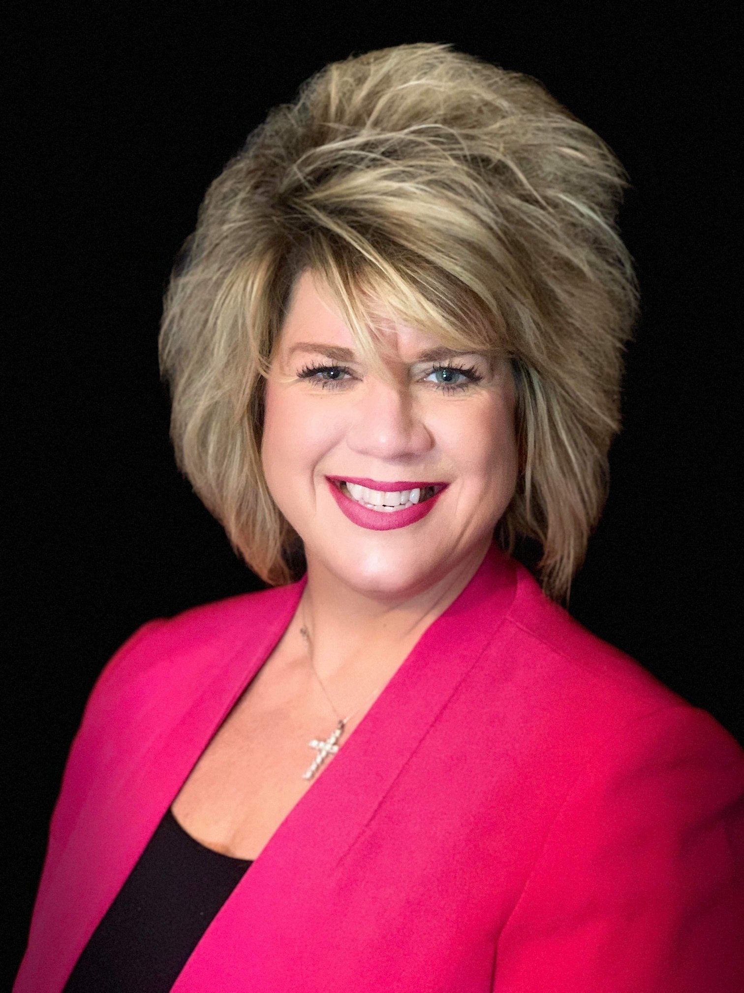 Woman with blonde, styled hair in a pink blazer smiles at the camera.