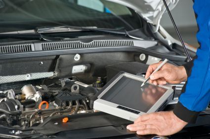 Mechanic using a diagnostic tablet on a car engine in a garage.