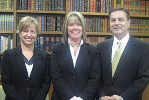 A man and two women are posing for a picture in front of a bookshelf.