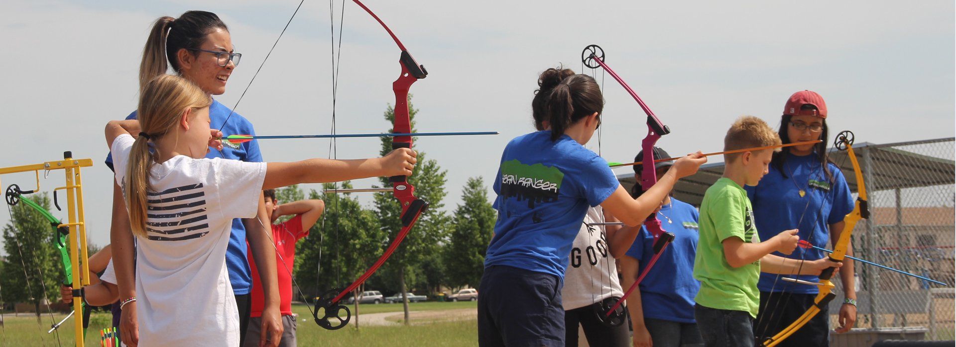 A group of children are standing in a field holding bows and arrows.