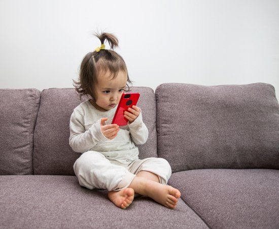 A little girl is sitting on a couch looking at a cell phone.